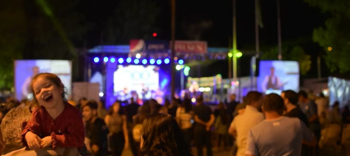 Una niña ríe desde los hombros de su padre, mirando el escenario iluminado de la fiesta de noche
