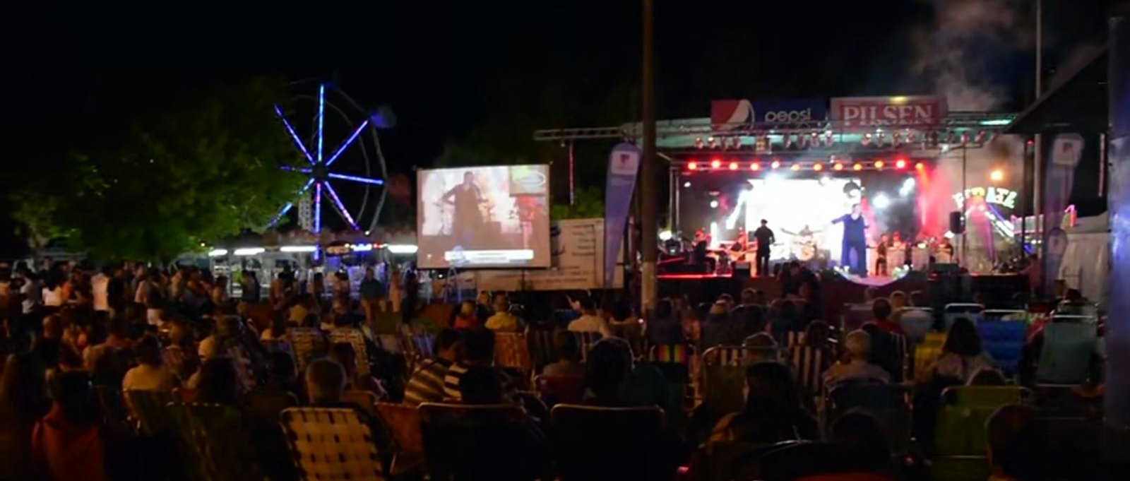Escenario principal iluminado con público colmado y la rueda de la fortuna girando de fondo